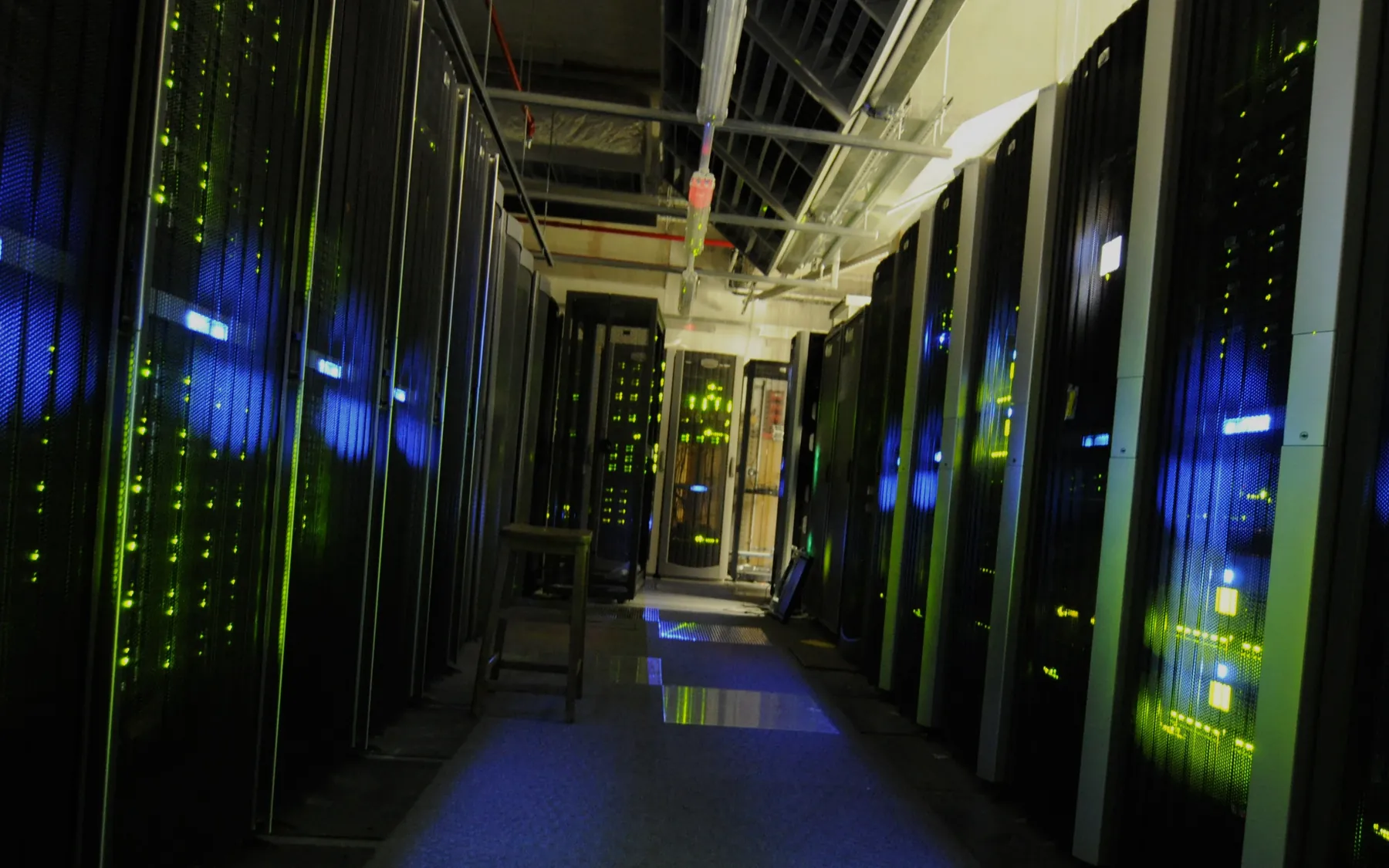 A dark aisle between server racks in a data centre, with glowing blue and green lights.